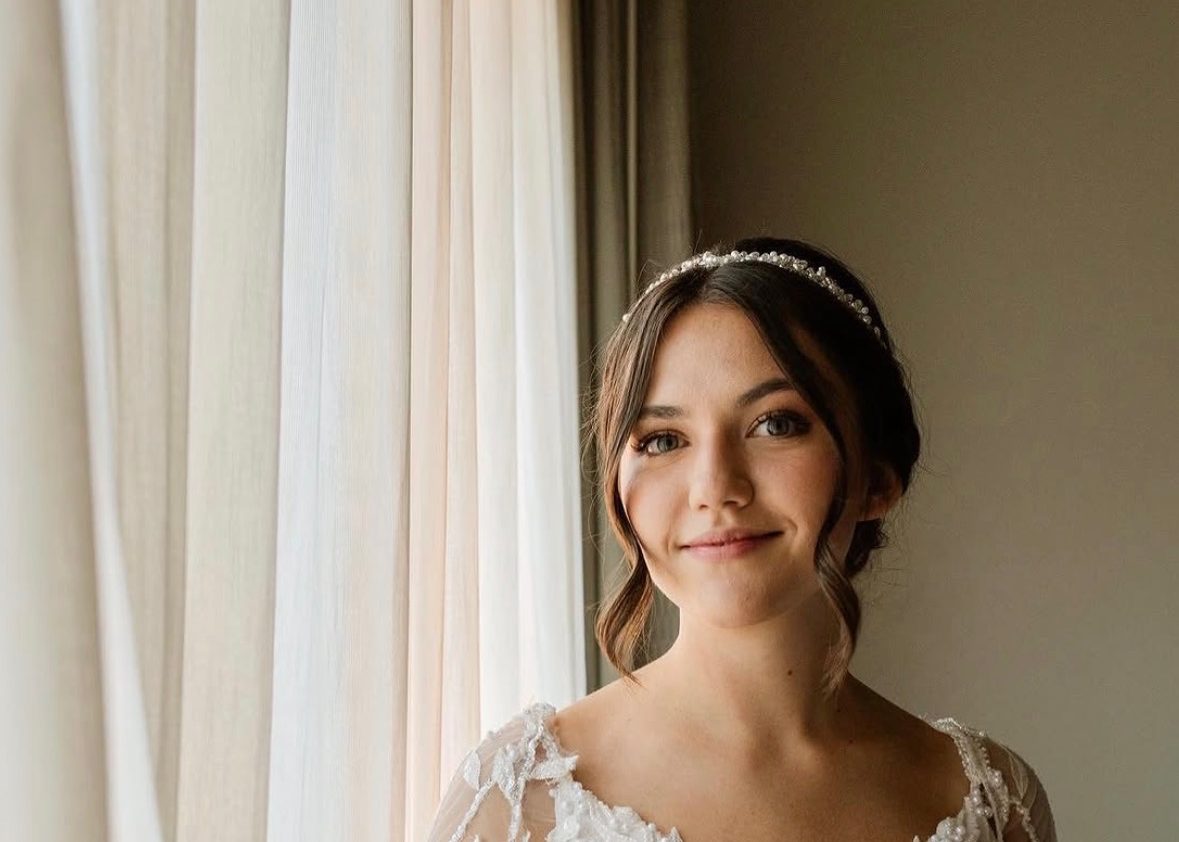 Bride in a beaded gown and pearl headpiece by a window, soft romantic bridal makeup
